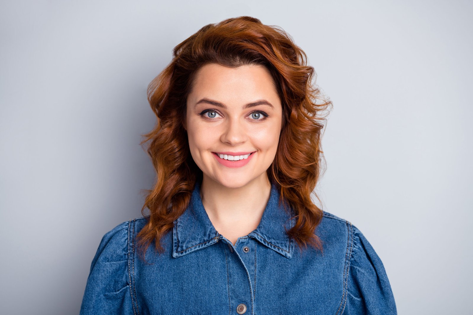 A smiling young white woman with curled red hair wearing a denim shirt.