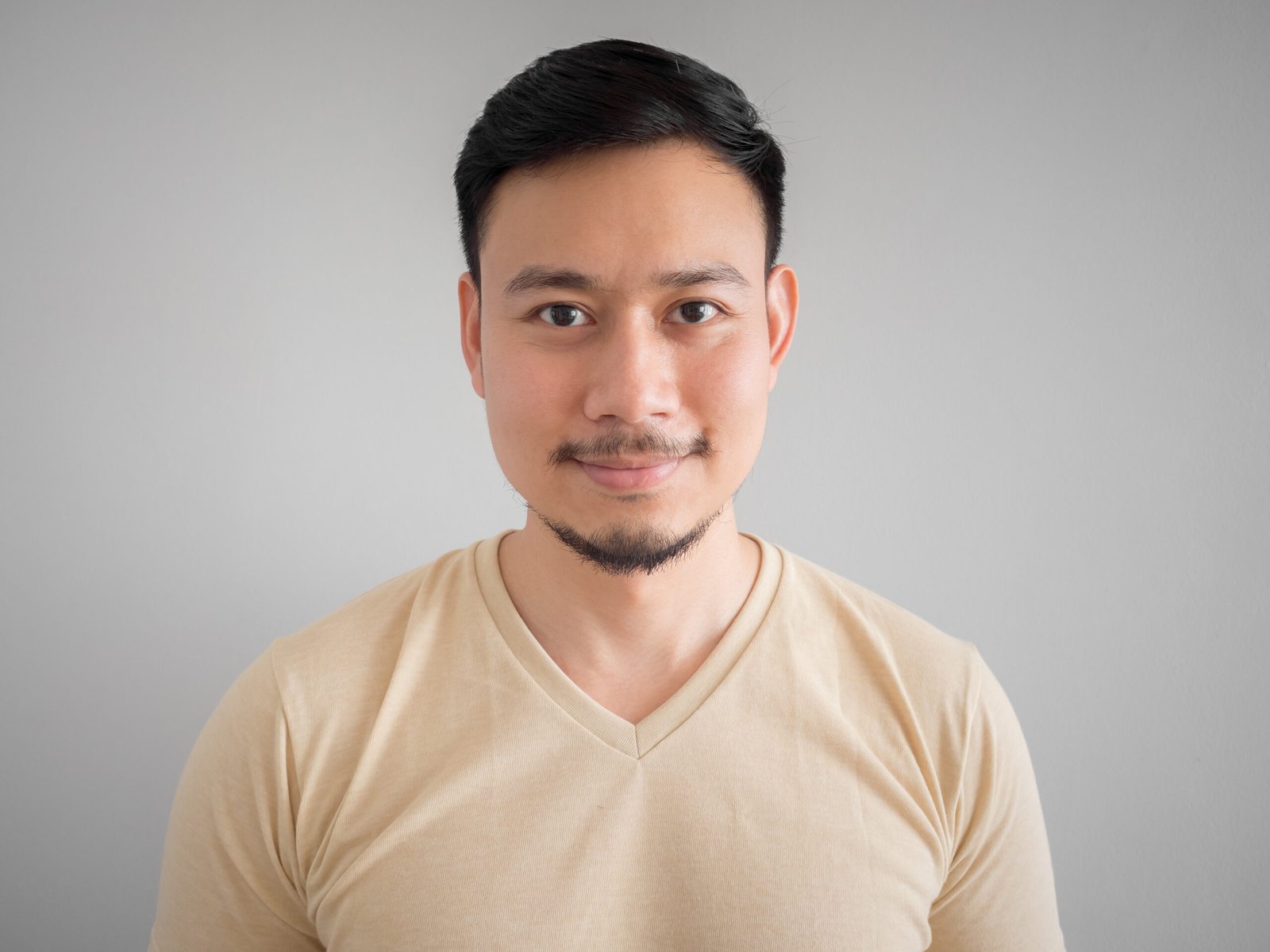 Headshot of young smiling Asian man with facial hair.