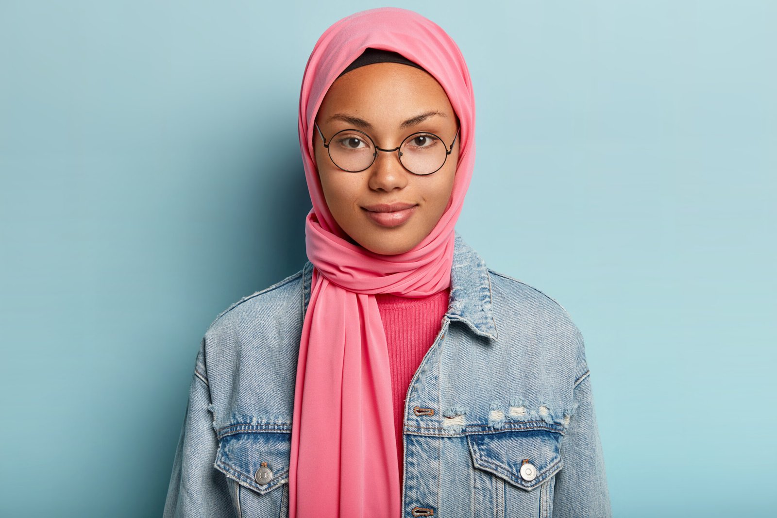 A young looking mixed race woman wearing glasses and a pink headscarf