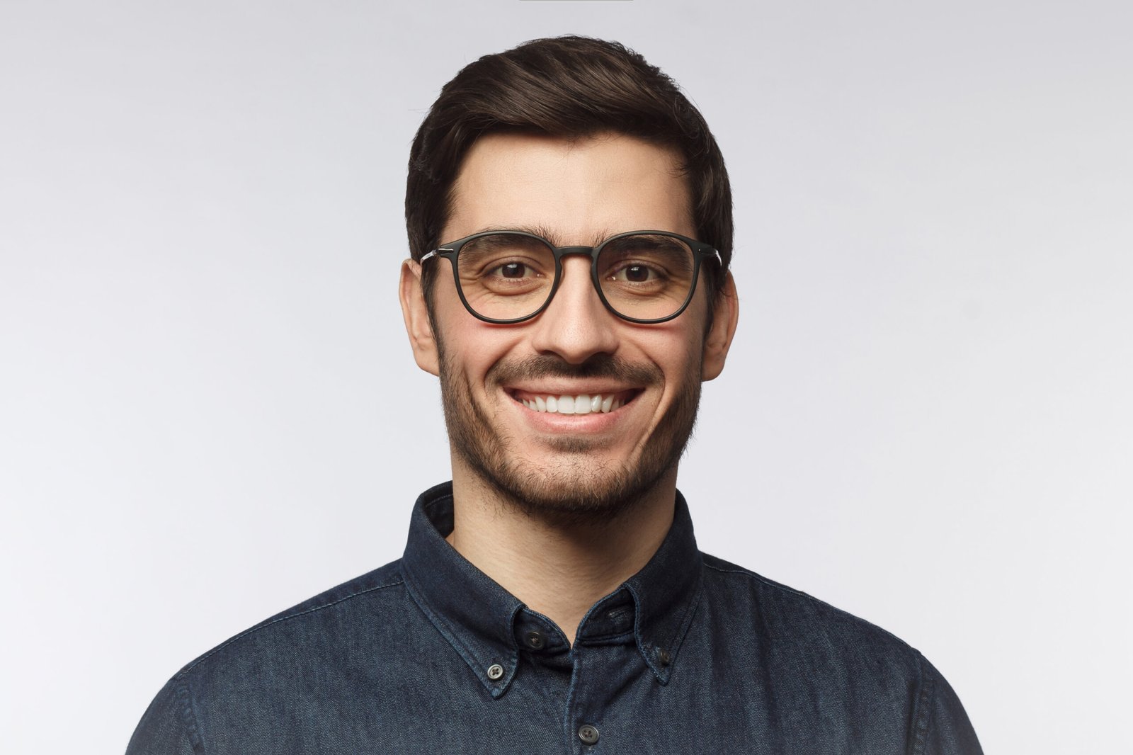 Young smiling man with short dark hair and facial hair, wearing glasses.