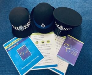 Three ADHD awareness raising posters and the ADHD in Custody guide are spread out on a blue carpet below three police hats from Cumbria Constabulary.